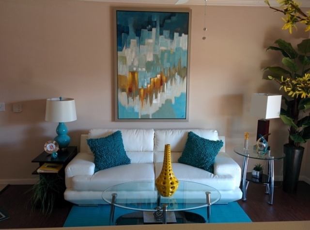 White couch with blue fluffy pillows and contemporary colorful blue and gold painting above
